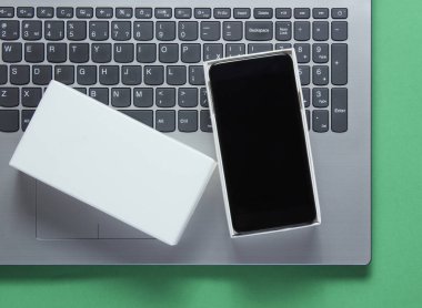 Paketleri açma, tekno blog yazma kavramı. Yeni akıllı telefon kutusu, yeşil arka planda dizüstü bilgisayar.