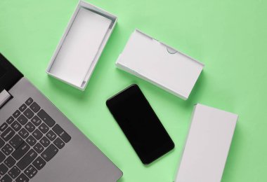 Boksu açma, tekno blog yazma kavramı. Yeni akıllı telefonlu bir kutu, pastel yeşil arka planda dizüstü bilgisayar. Üst görünüm