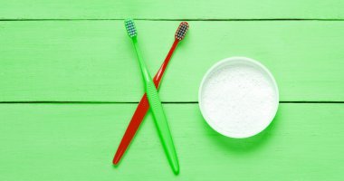 İki diş fırçası, yeşil ahşap arka planda diş pudrası. Minimalizm ağız temizliği kavramı. Üst görünüm