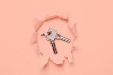 Bunch of metal keys through a torn hole on vanilla pink paper background