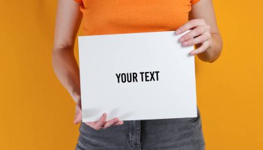 Sarı arka planda, fotokopi alanı için beyaz boş kağıt tutan bir kadın. Ekin fotoğrafı, stüdyo fotoğrafı.