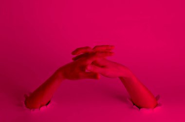 Woman stretches her fingers through the torn holes with pink neon light. Creative art