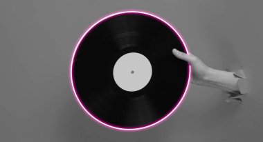Female hand holding vinyl record with neon circle through the torn paper background.