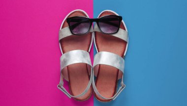 Creative summer beach flat lay. Leather women's sandals, sunglasses on colored background. Top view