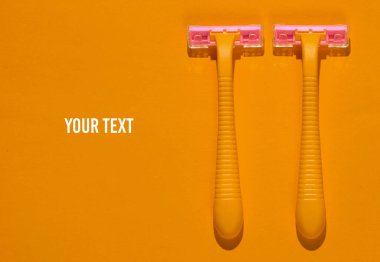 Two plastic razors on yellow background. Minimalistic beauty and fashion concept. Copy space