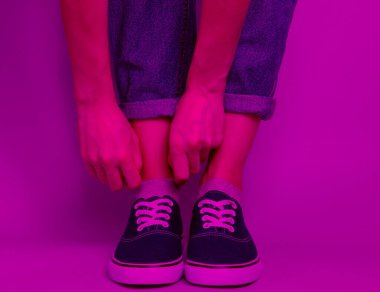 Moda stüdyo çekimi. Kot pantolonlu ve spor ayakkabılı kadın çorabını yırtıyor. Pembe neon ışık