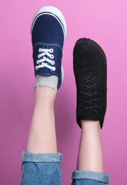 Pantolonlu kadın bacakları, çizmeli ayakkabıları ve pembe pastel arka planda spor ayakkabıları. Mevsimlik ayakkabılar. Yaratıcı moda çekimi