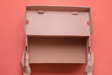 Kadın eli pembe arka planda boş bir karton kutu tutuyor. Üst görünüm