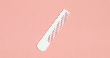 Pembe pastel arka planda beyaz plastik tarak. Saç bakımı, güzellik konsepti. Üst görünüm