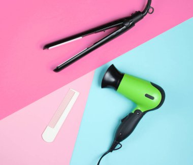 Minimalist güzellik ve moda hala hayat. Renkli arka planda saç kurutma makinesi, tarak ve saç düzleştiricisi. Üst manzara, düz uzanma