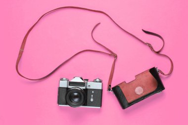 Turist minimalizmi. Eski moda film kamerası ve pembe arka planda kayışı olan deri kapaklı. Üst görünüm