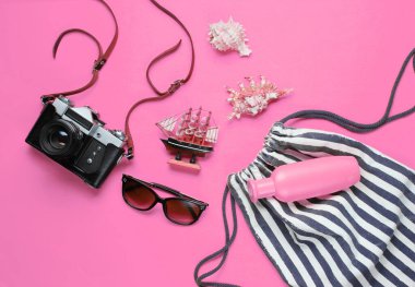 Gezgin aksesuarları, pembe arka planda retro kamera. Sahilde gezi, tatil. Yaz minimalist geçmişi. Düz yatay turizm alegorisi