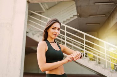Spor giyim sektöründe çekici bir kadın şehir ortamında akıllı saat kullanıyor.