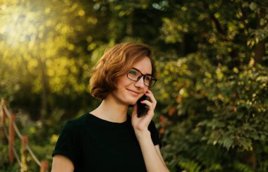 Gözlüklü genç hippi dışarıda telefonla konuşuyor.