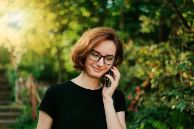 Gözlüklü genç hippi dışarıda telefonla konuşuyor.