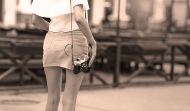 Kentsel çevrede aşınabilir giysiler içindeki bir kadının omzunda asılı duran eski bir kamera.