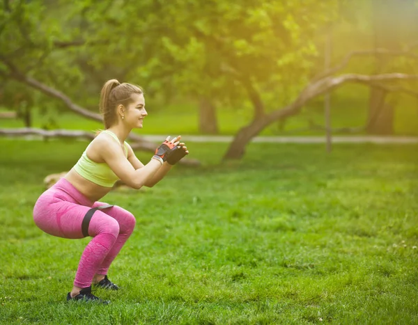 Sportowa Kobieta Robi Przysiady Ekspanderem Gumy Fitness Parku Świeżym Powietrzu — Zdjęcie stockowe