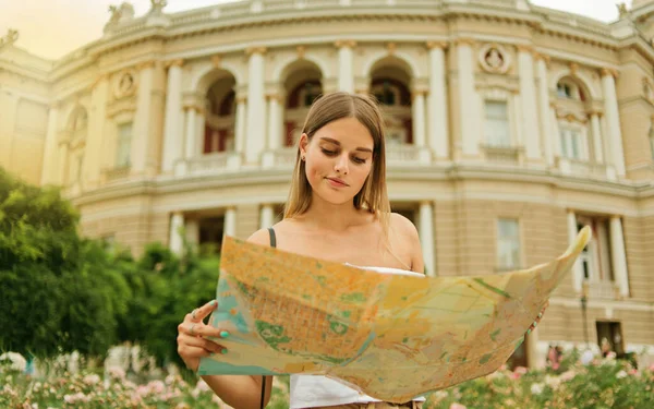 混乱した女性の観光客は 観光都市の建築の背景に都市の彼女の手の地図で保持しています 新しい場所への旅行 — ストック写真