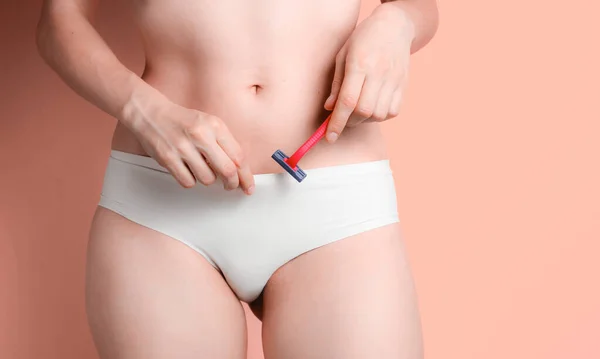 Slim woman with perfect body in panties holds razor on pink background. The concept of care for your body, the epilation of non-residential hair