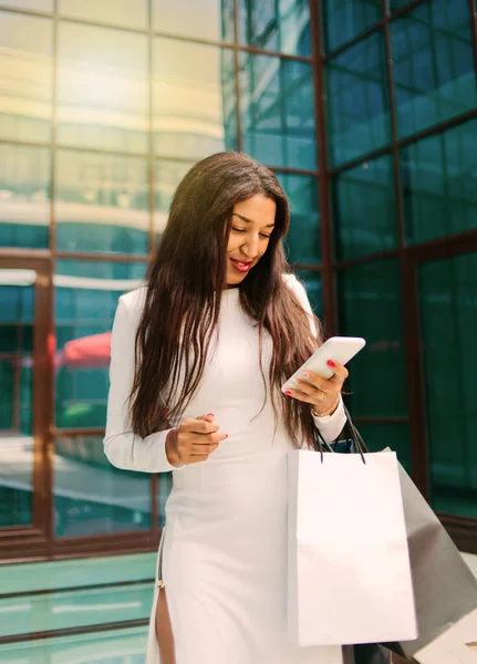 Młoda Afro Kobieta Białej Sukience Papierowymi Torbami Zakupy Używać Smartfona — Zdjęcie stockowe