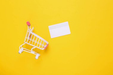 Sarı arka planda banka kartı olan mini alışveriş arabası. Üst görünüm