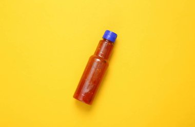 Sarı arka planda bir şişe domates sosu (ketçap).