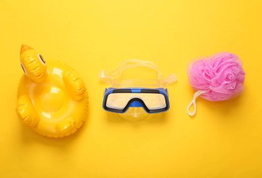 Banyo için çocuk aksesuarları ve oyuncaklar. Dalış maskesi, ördek ve sarı arka planda bez. düz yat