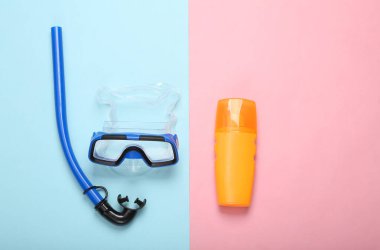 Yaz tatili. Dalış seti ve mavi pembe pastel arka planda güneş kremi. Minimum plaj tatili konsepti