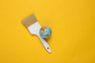Sarı arka planda küreyle boya fırçası. Yaratıcı yerleşim
