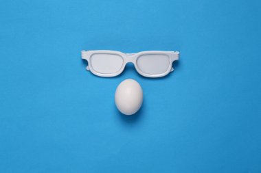 Mavi arka planda yumurta olan beyaz gözlükler. Yaratıcı yerleşim
