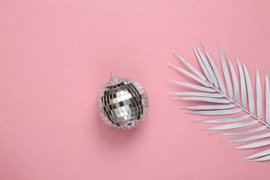 Asgari yaratıcı düzen. Parti konsepti. Pembe pastel arka planda beyaz palmiye yaprağı olan disko topu. Üst görünüm