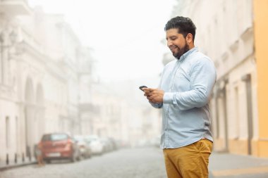Sisli bir Avrupa caddesinde telefon kullanan neşeli İspanyol genç adam.