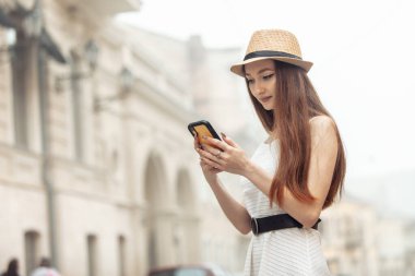 Şapkalı hoş beyaz kadın Avrupa caddesinde akıllı telefon kullanıyor.