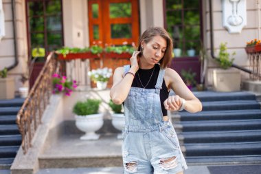 Kot pantolon giymiş şık bir kadın şehirdeki saat tuşlarına bakıyor.