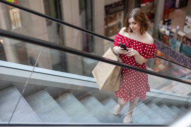 Kırmızı benekli elbiseler içinde alışveriş merkezlerinde telefon kullanan sevimli bir kadın.