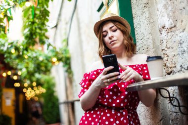 Puantiyeli elbiseli genç bayan sokak kafesinde akıllı telefon kullanıyor.