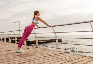 Sıska, fit bir kadın sahildeki korkuluklardan yukarı itin.