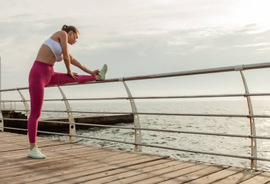 Güzel, formda bir kadın sahilde bacak esneme egzersizi yapıyor.