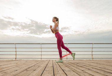 Spor giyim trenlerinde, plajda spor lastikleri olan güzel kızıl saçlı fitness mankeni. Sağlıklı yaşam tarzı