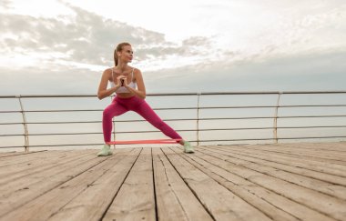 Spor giyim trenlerinde, plajda spor lastikleri olan güzel kızıl saçlı fitness mankeni. Sağlıklı yaşam tarzı