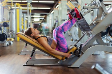 Spor giyimli güzel bir kadın modern spor salonunda bacak kaslarını egzersiz makinesinde çalıştırıyor. Sağlıklı bir yaşam tarzı. Güçlü vücut