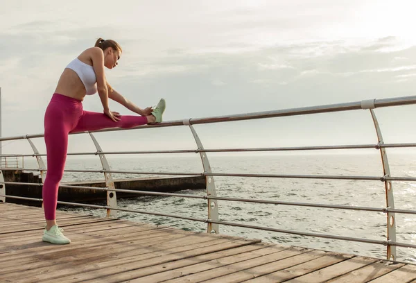 Güzel, formda bir kadın sahilde bacak esneme egzersizi yapıyor.