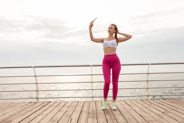 Vacker Rödhårig Träningsmodell Sportkläder Gör Selfie Smartphone Stranden — Stockfoto