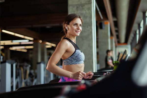 Young fit woman jogging on a treadmill in modern gym. Cardio workout