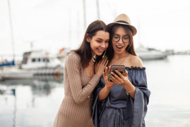 İki şaşkın bayan arkadaş yat kulübündeki akıllı telefon ekranına bakın.