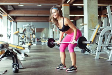 Atletik genç kadın spor salonunda halterle sırt kaslarını çalıştırıyor. Sağlıklı yaşam tarzı