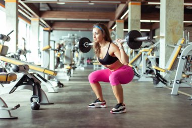 Sporcu güzel bir kadın spor salonunda omuzlarında halterle çömeliyor. Sağlıklı yaşam tarzı