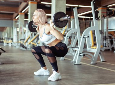 Sporcu güzel bir kadın spor salonunda omuzlarında halterle çömeliyor. Sağlıklı yaşam tarzı