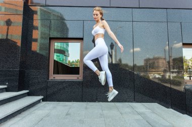Genç ve formda bir kadın şehir ortamında zıplama pratiği yapıyor.