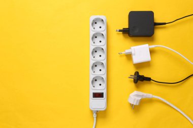 Sarı arka planda farklı prizleri ve adaptörleri olan elektrik uzatma kablosu. Üst görünüm.